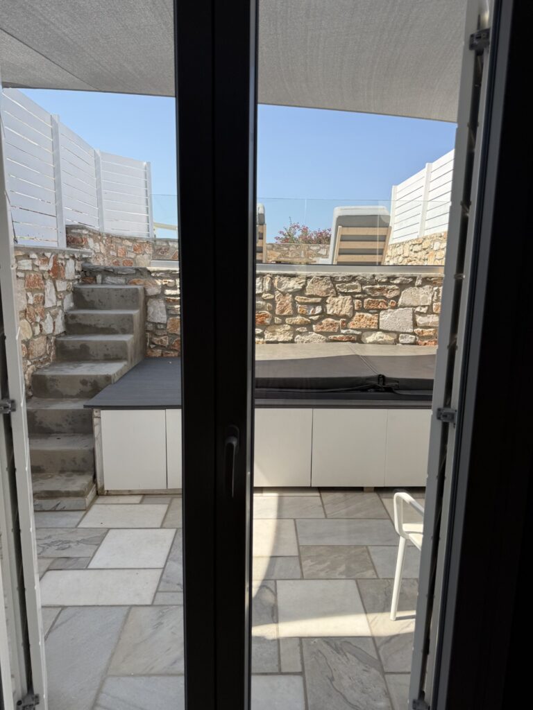 Covered outdoor jacuzzi and private terrace seen through our room doors at Paros Agnanti Resort