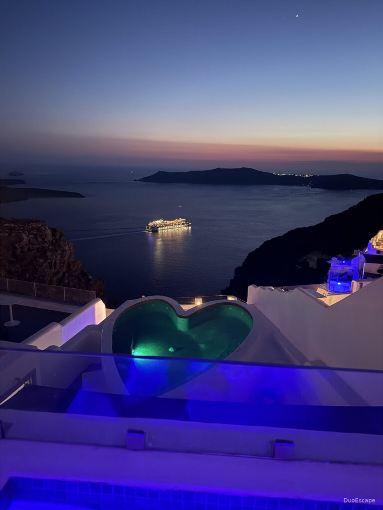 Illuminated heart-shaped pool with Santorini caldera view at twilight at Pegasus Suites and Spa